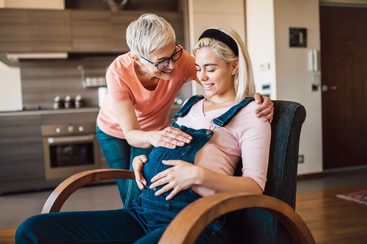 Young pregnant woman allowing friend to touch her belly