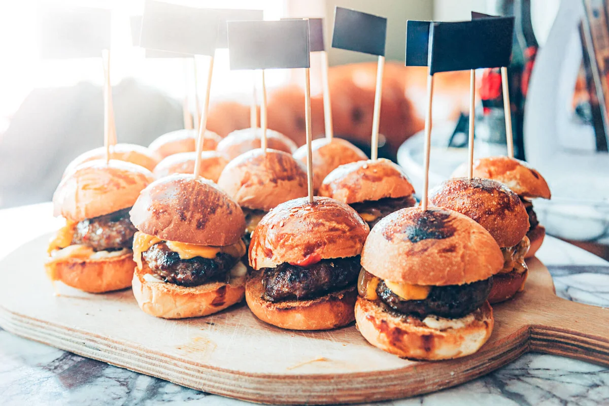 Assorted mini delicious cheeseburger sliders with cheese, onion and sauces with blank paper flag picks on wooden flag