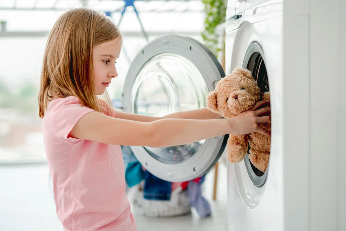 Little girl putting toy into washing machine