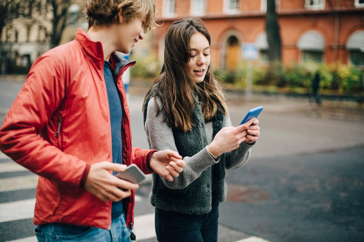 Girl talking while showing mobile phone to male friend on city street