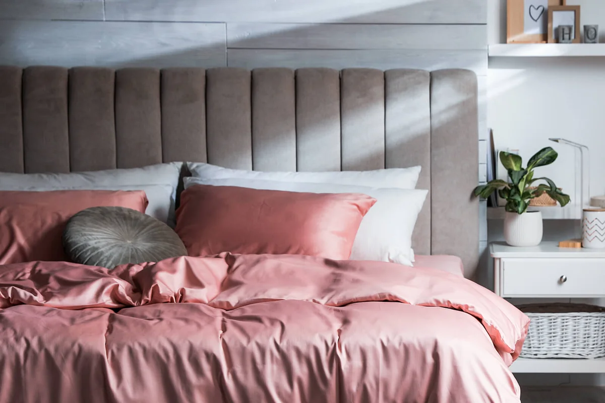 Bed with beautiful silky linens in stylish room interior