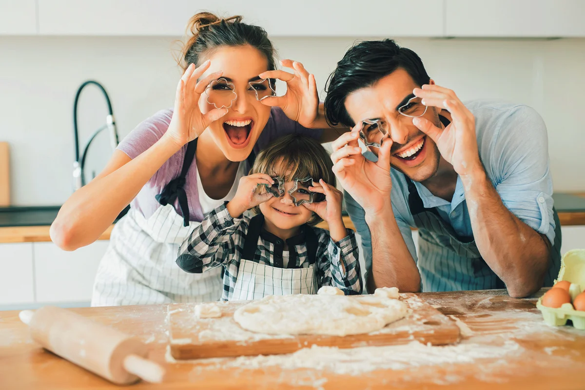 Young family holding cookie cutters in front of their eyes while making cookies in the kitchen.