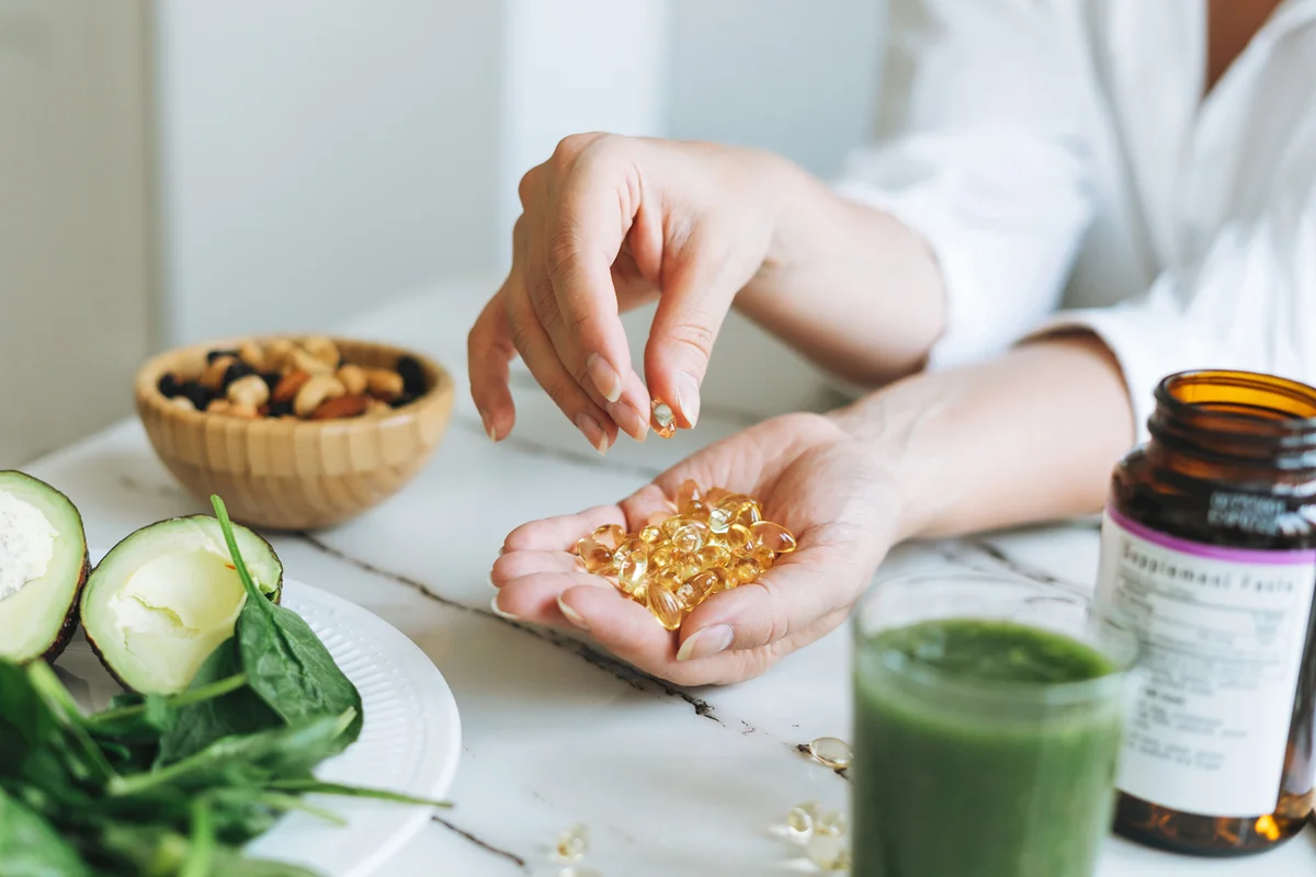 Woman Hands In White With Omega 3, Vitamin D Capsules With Green Vegan Food