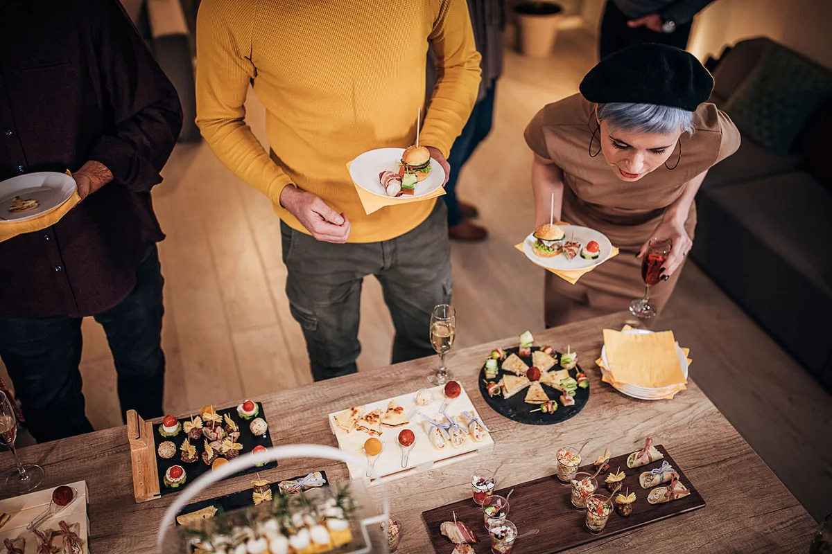 Colleagues sampling savory dishes from buffet table at office party