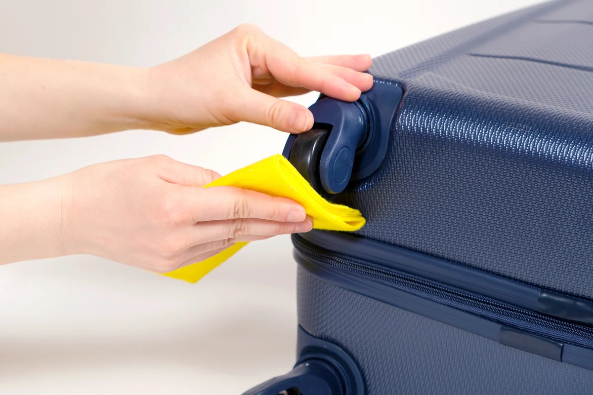 Cleaning the rubber wheels of a travel suitcase with a yellow rag