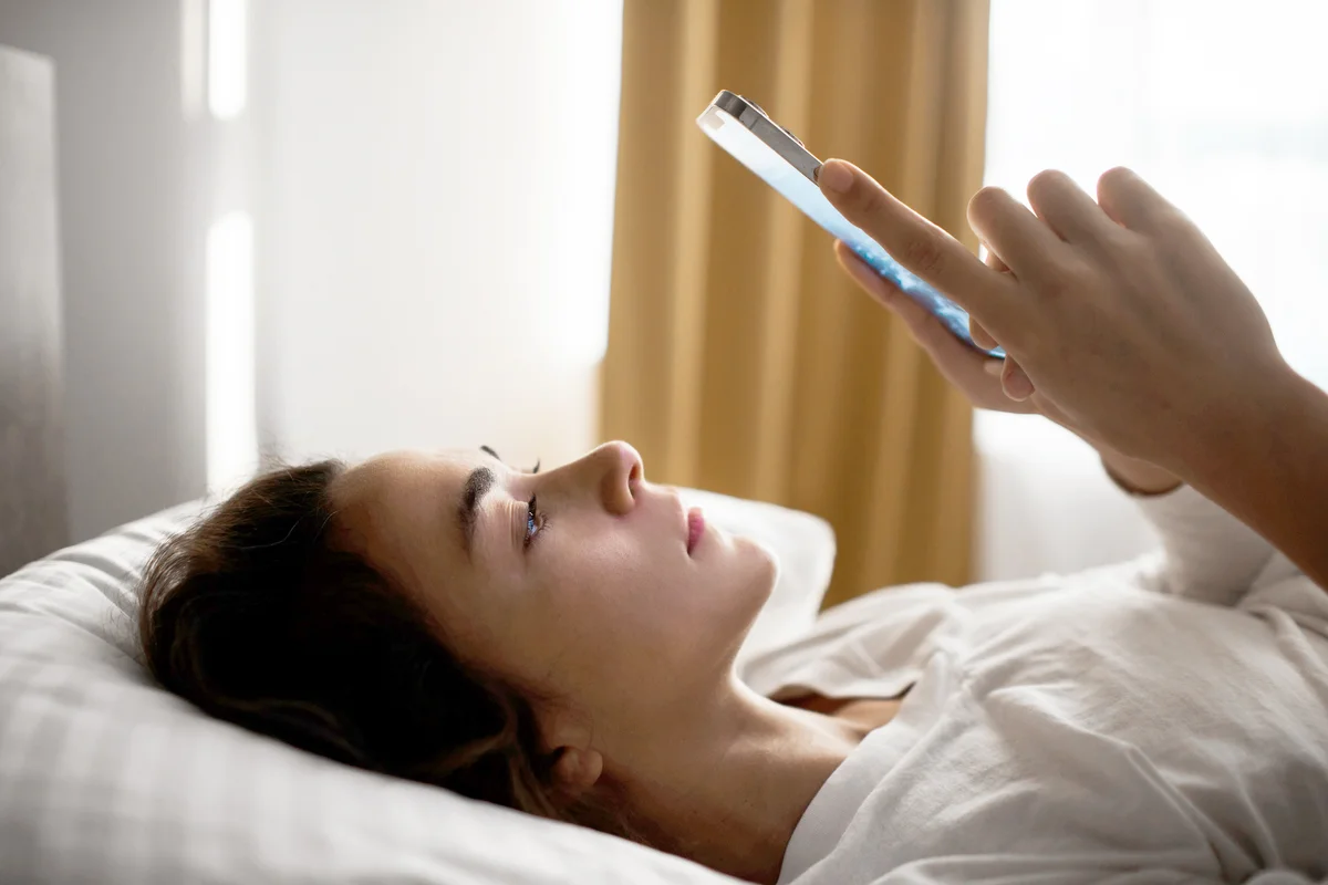 Sad and tired woman lying in bed while texting