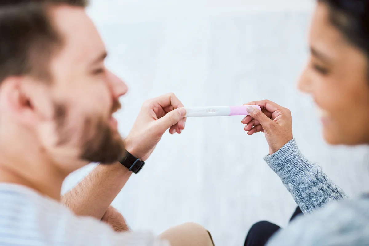 Happy young couple sitting on the sofa together and holding a positive pregnancy test