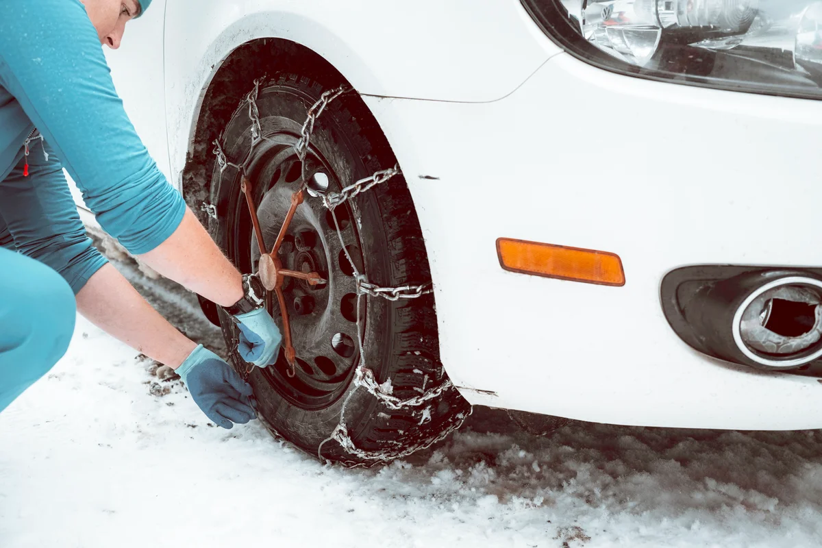 A women instals snow tire chains on a car