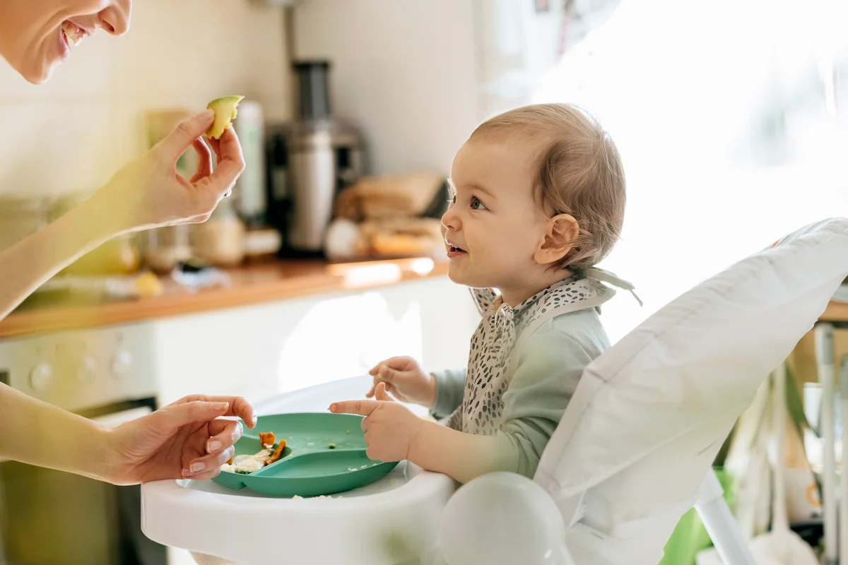 Excited baby girl looking at mother holding food