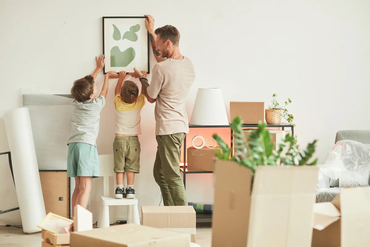 Happy father with two sons hanging pictures on wall while moving in to new home