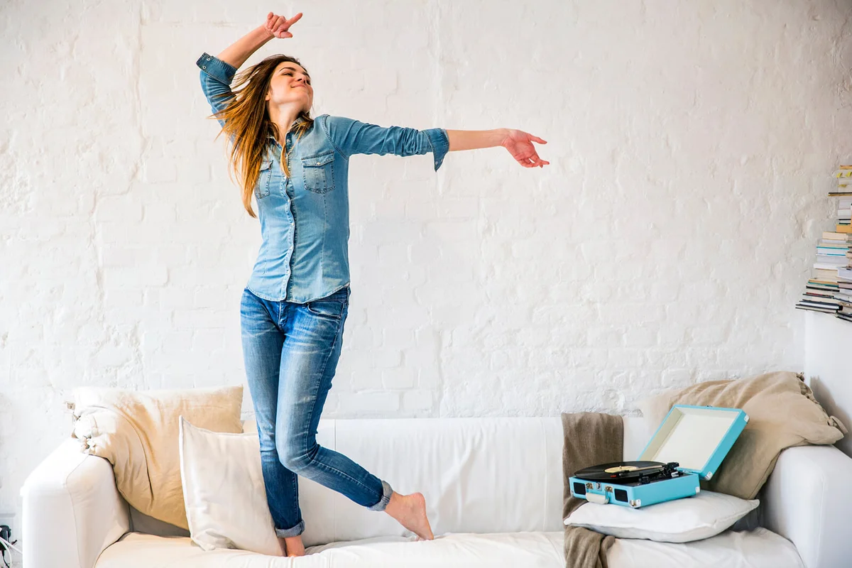 woman standing on sofa dancing to vintage record player