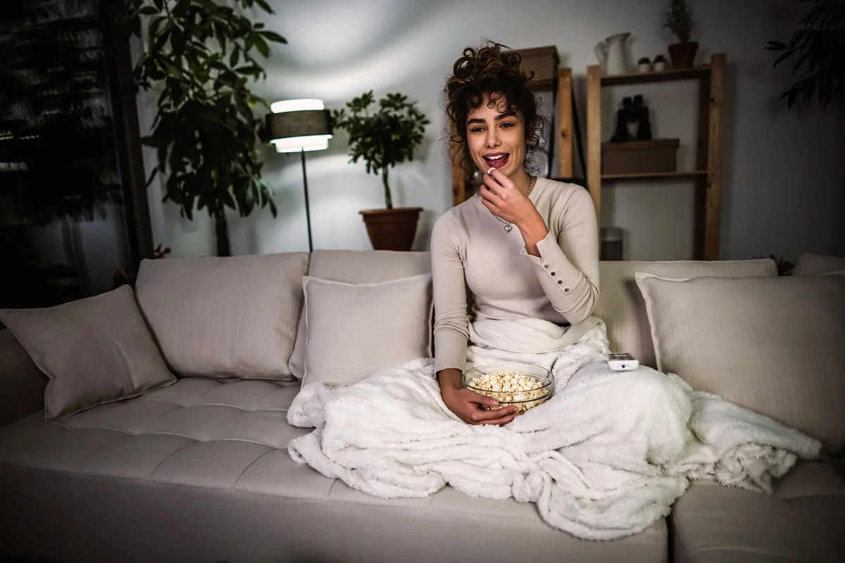 Young woman eating popcorn and watches movie on TV