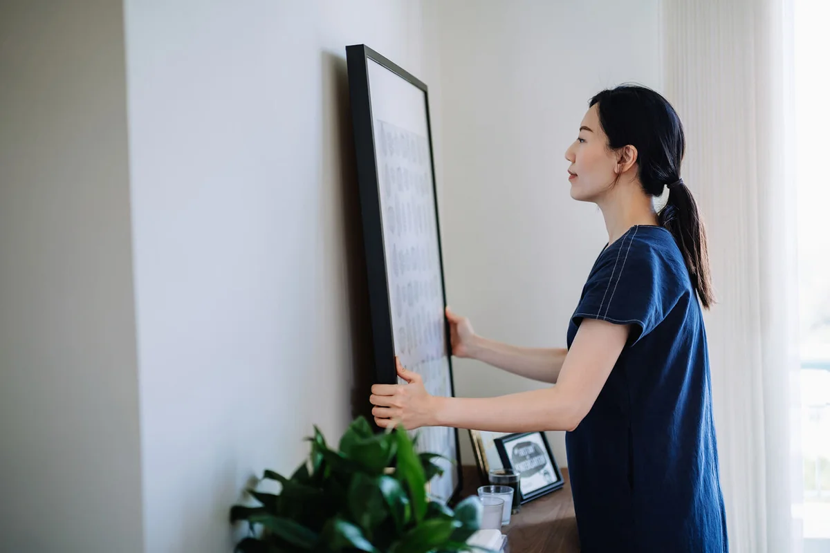 woman hanging picture frame on the wall decorating living room at home