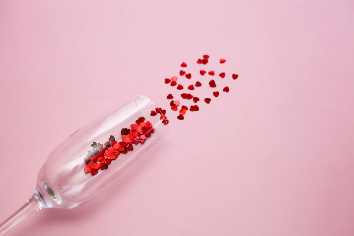 Flat lay of champagne glass with red heart confetti