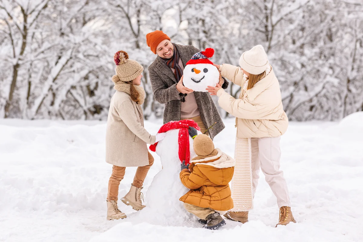 Happy children sculpting funny snowman together with parents in winter
