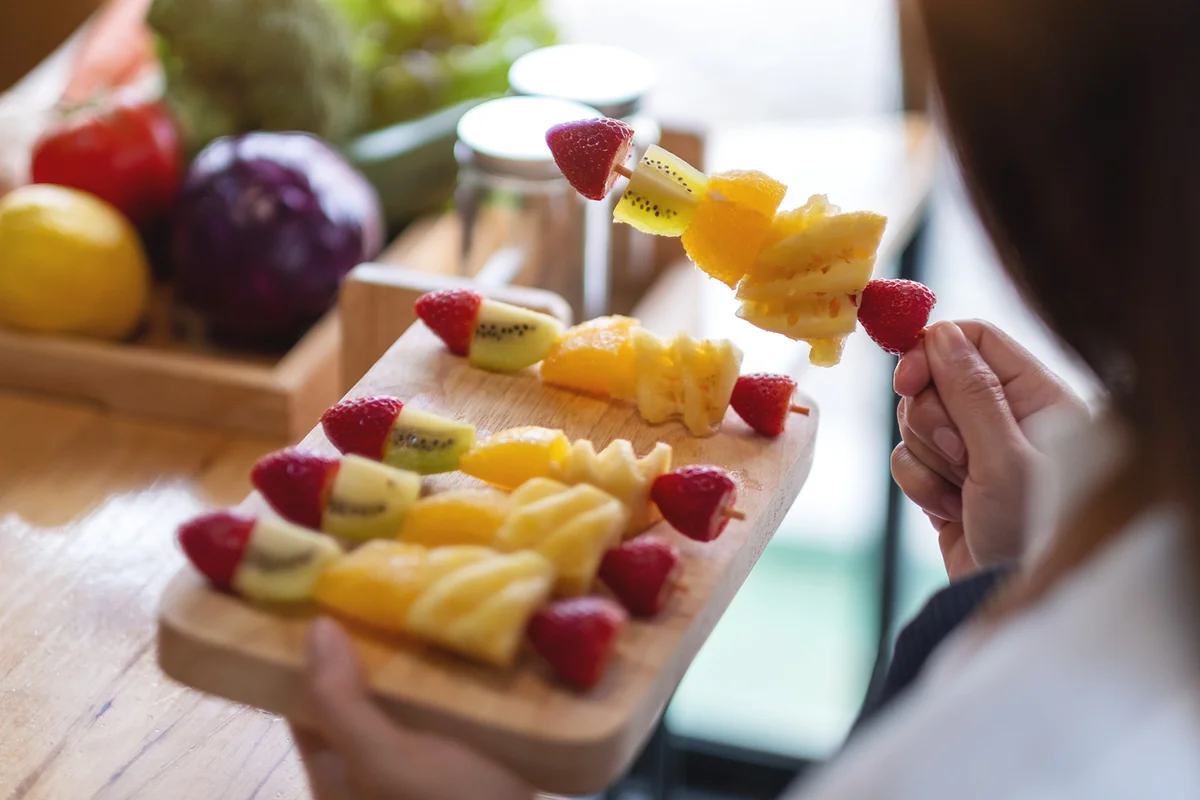 A female chef holding fresh mixed fruits on skewers in a wooden plate