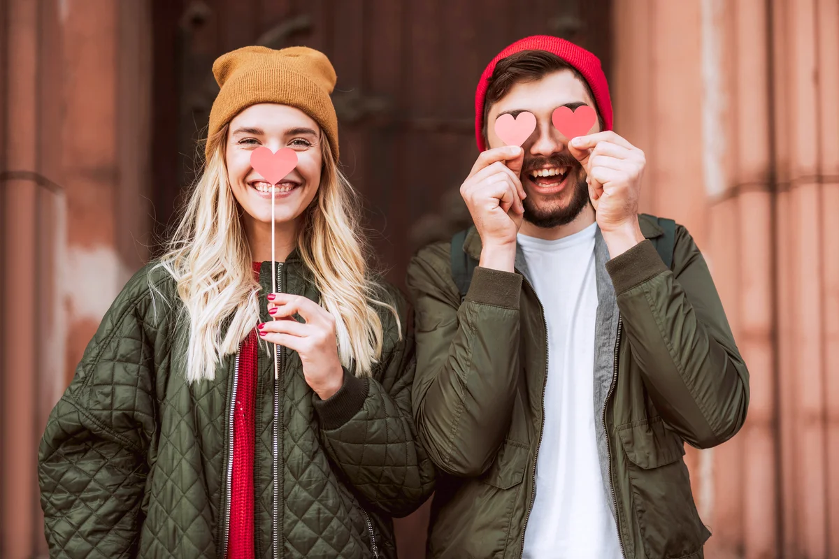 Beautiful young couple hiding behind red paper hearts