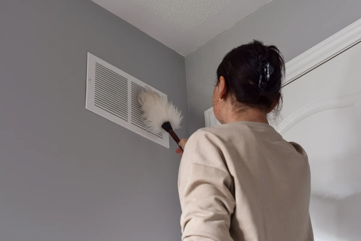 Woman cleaning return air vent with duster