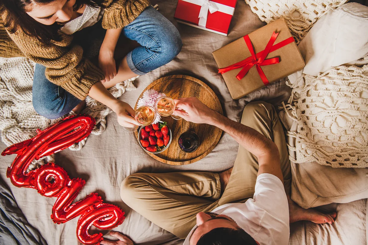 Young couple sitting in bed, giving presents drinking rose champagne