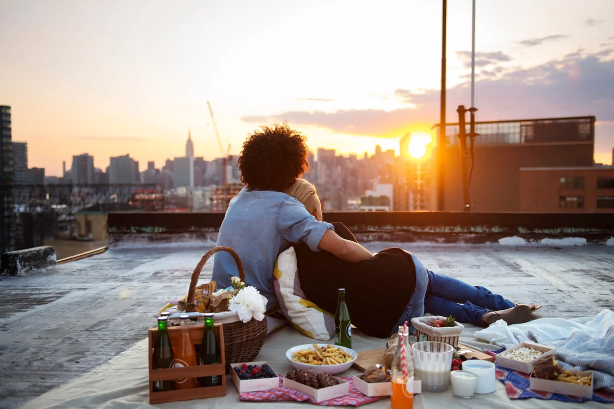 Couple relaxing on rooftop against sky during picnic