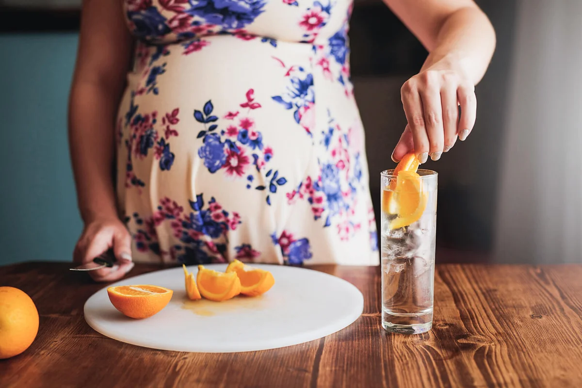 pregnant woman preparing a healthy drink with oranges at home