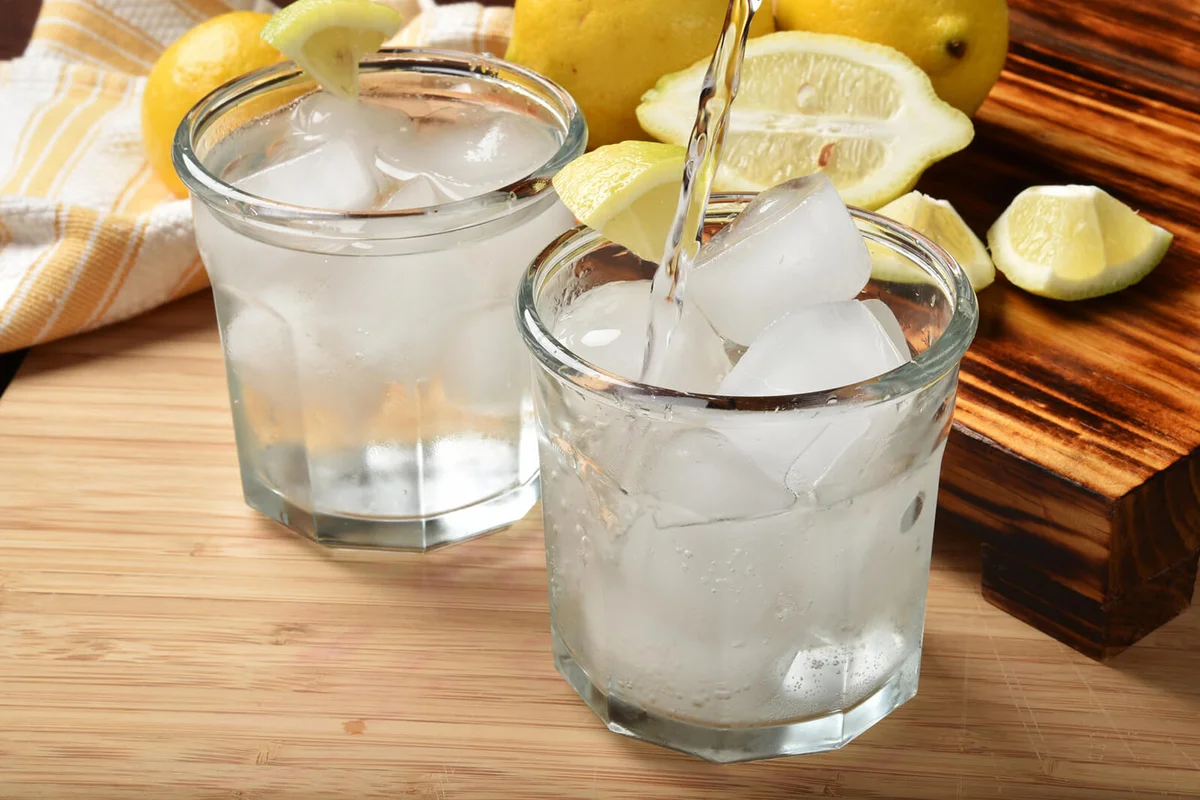 Pouring sparkling water into a glass with lemon wedges