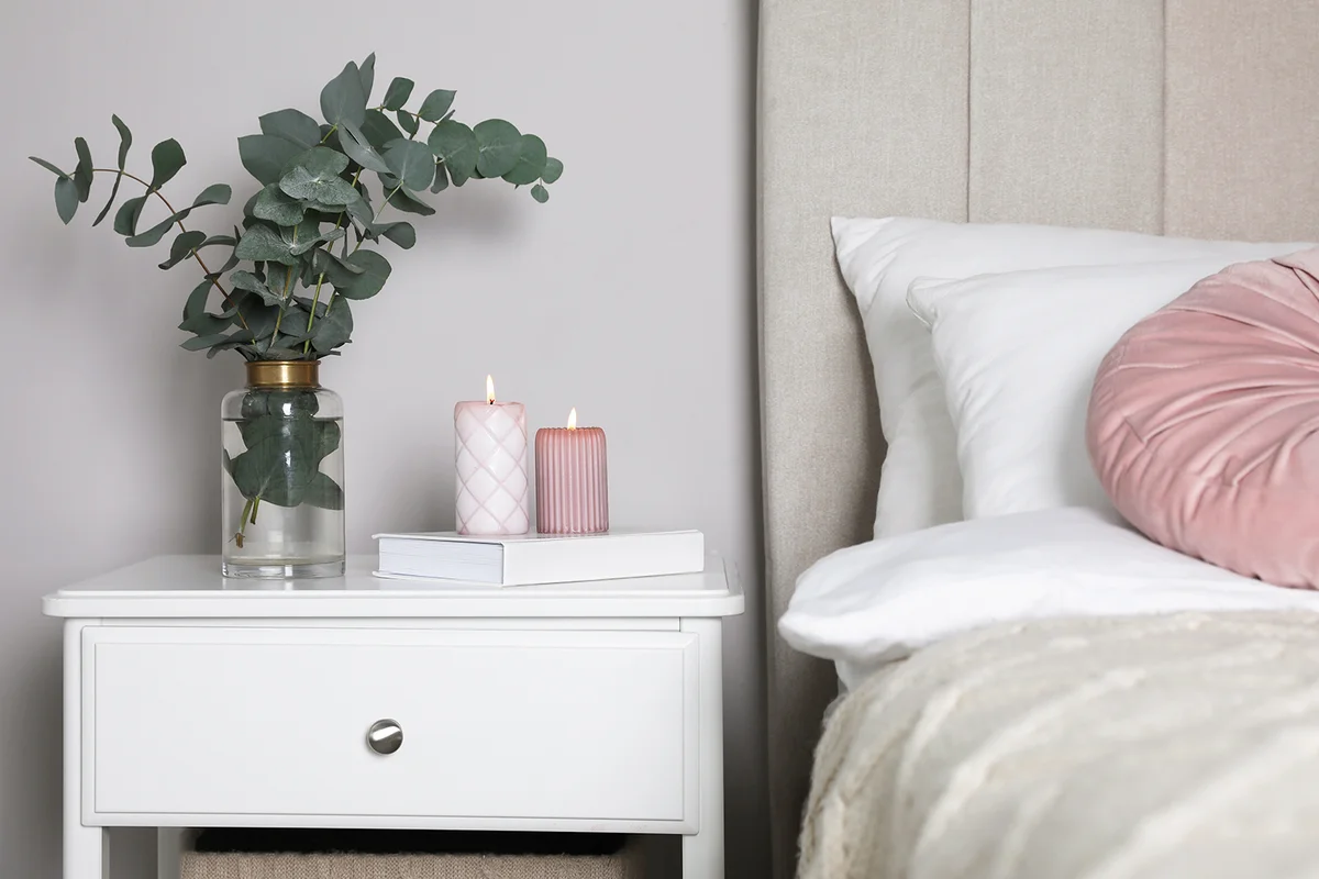 Vase with beautiful eucalyptus branches, book and candles on nightstand in bedroom