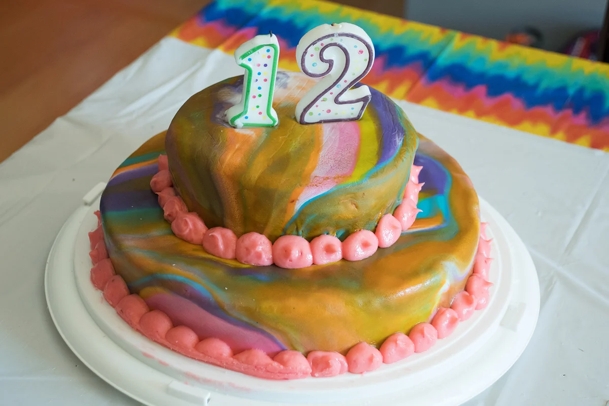 2th birthday cake with candles and tie dye fondant and pink frosting on tie dye tablecloth