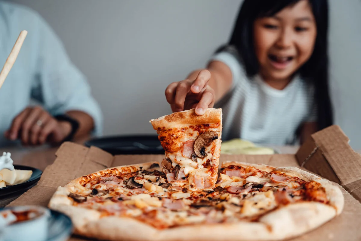 Cheerful Young Girl Holding A Slice Of Pizza