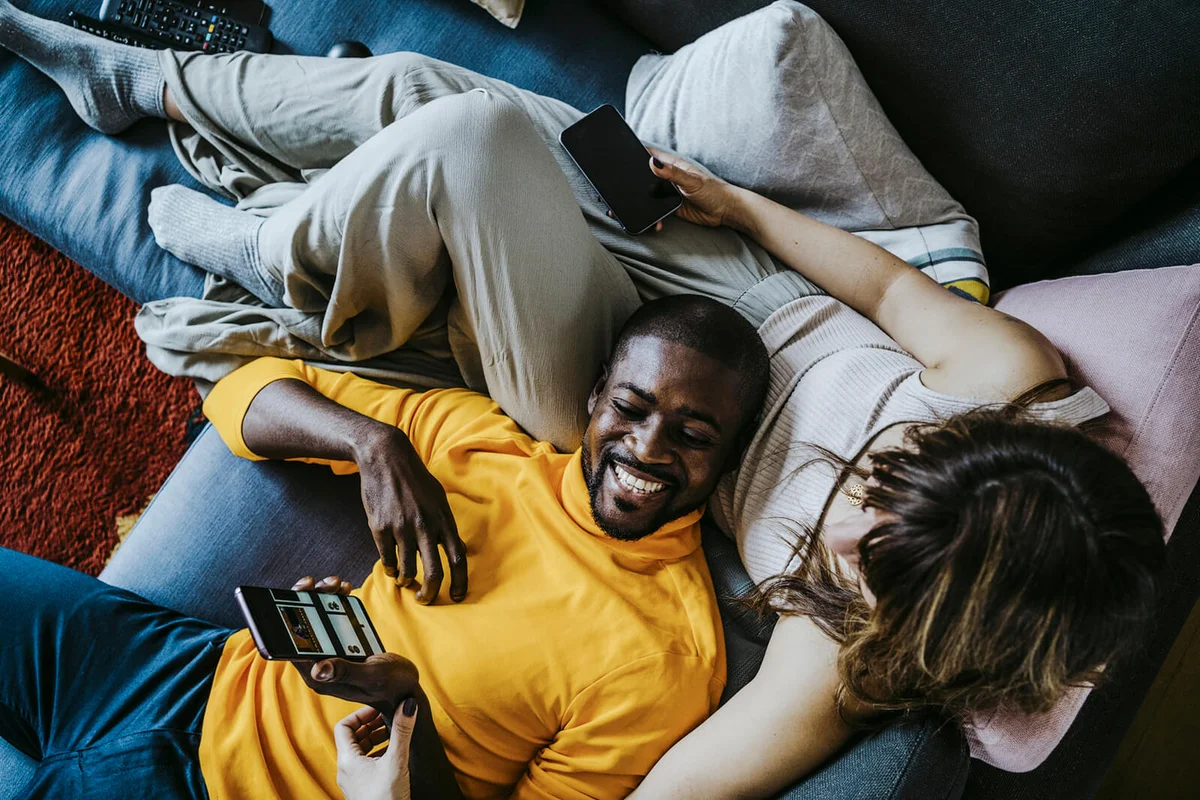 Cheerful man lying on sofa with girlfriend sitting in living room at home