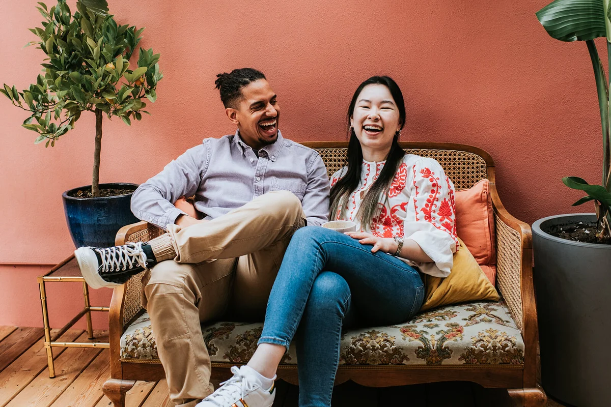 young couple sit on a sofa and laugh together