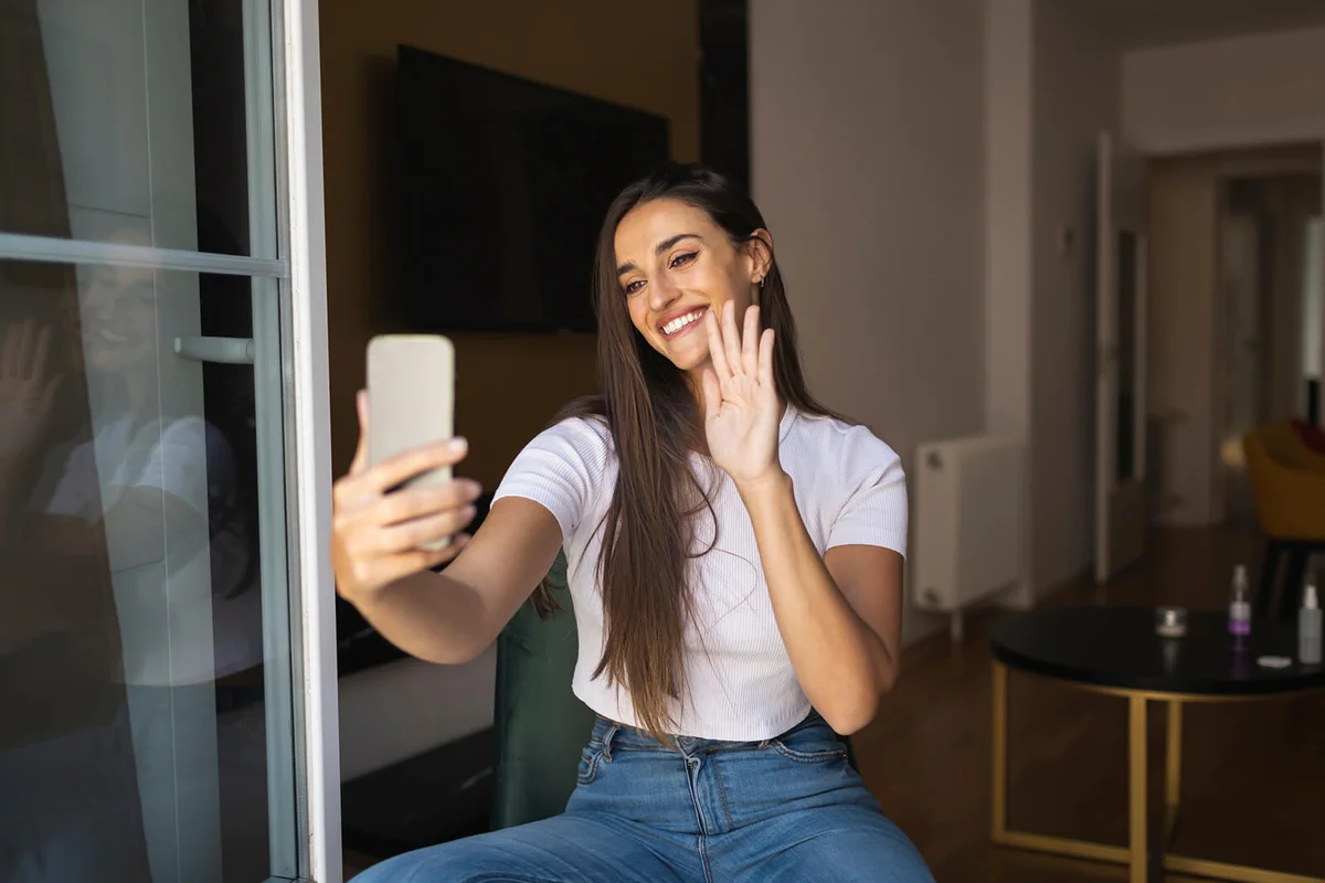 Smiling young woman waving hand during video call