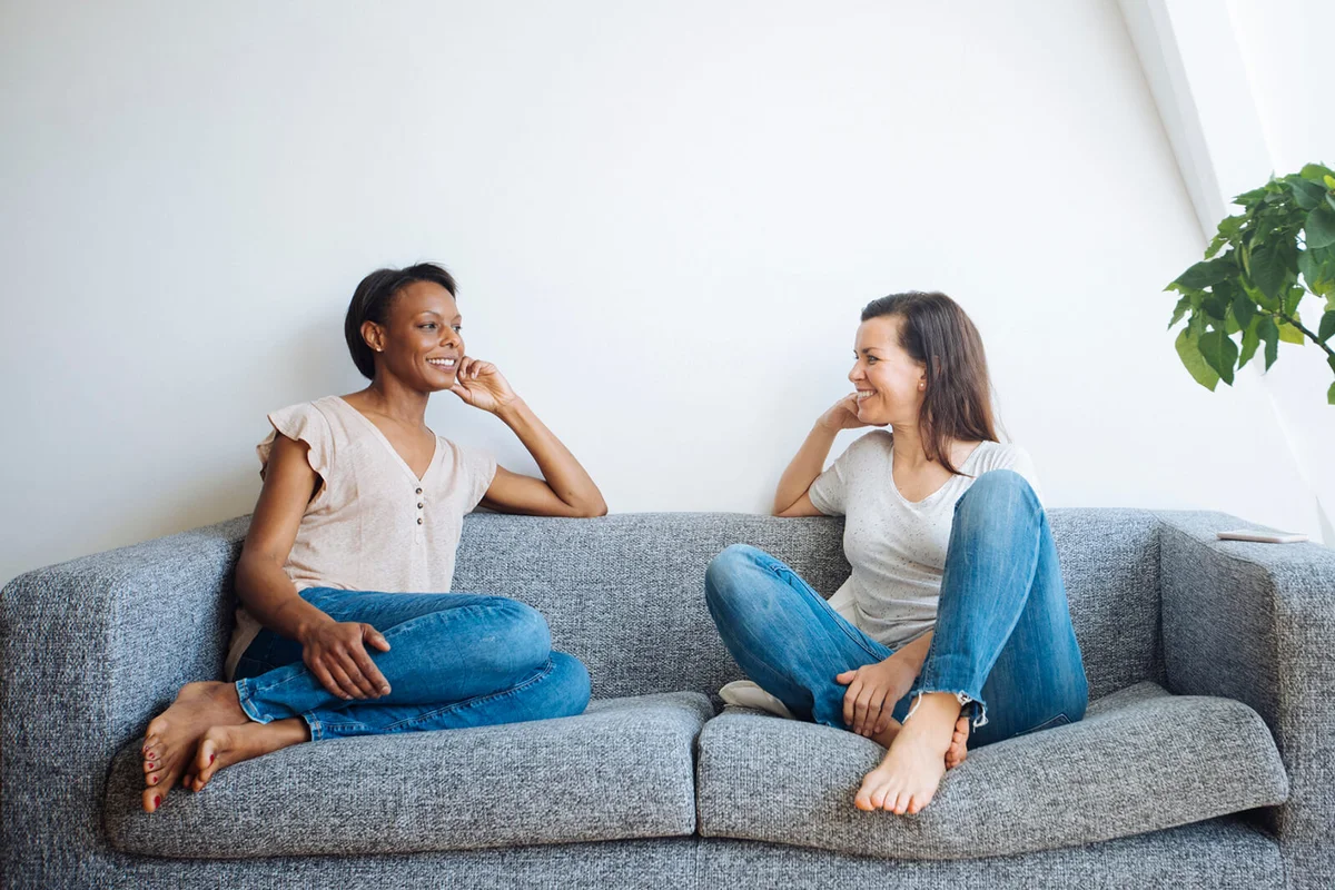 Two relaxed women sitting on couch at home talking