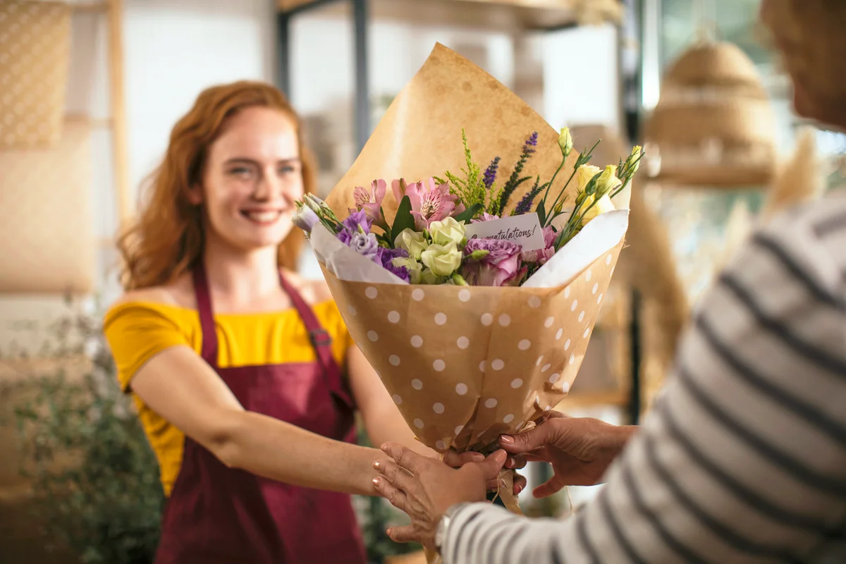 Young redhead woman giving her customer a beautiful bouquet of flowers