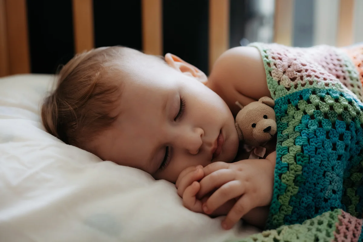 Cute baby sleeps peacefully in crib with handle under his cheek