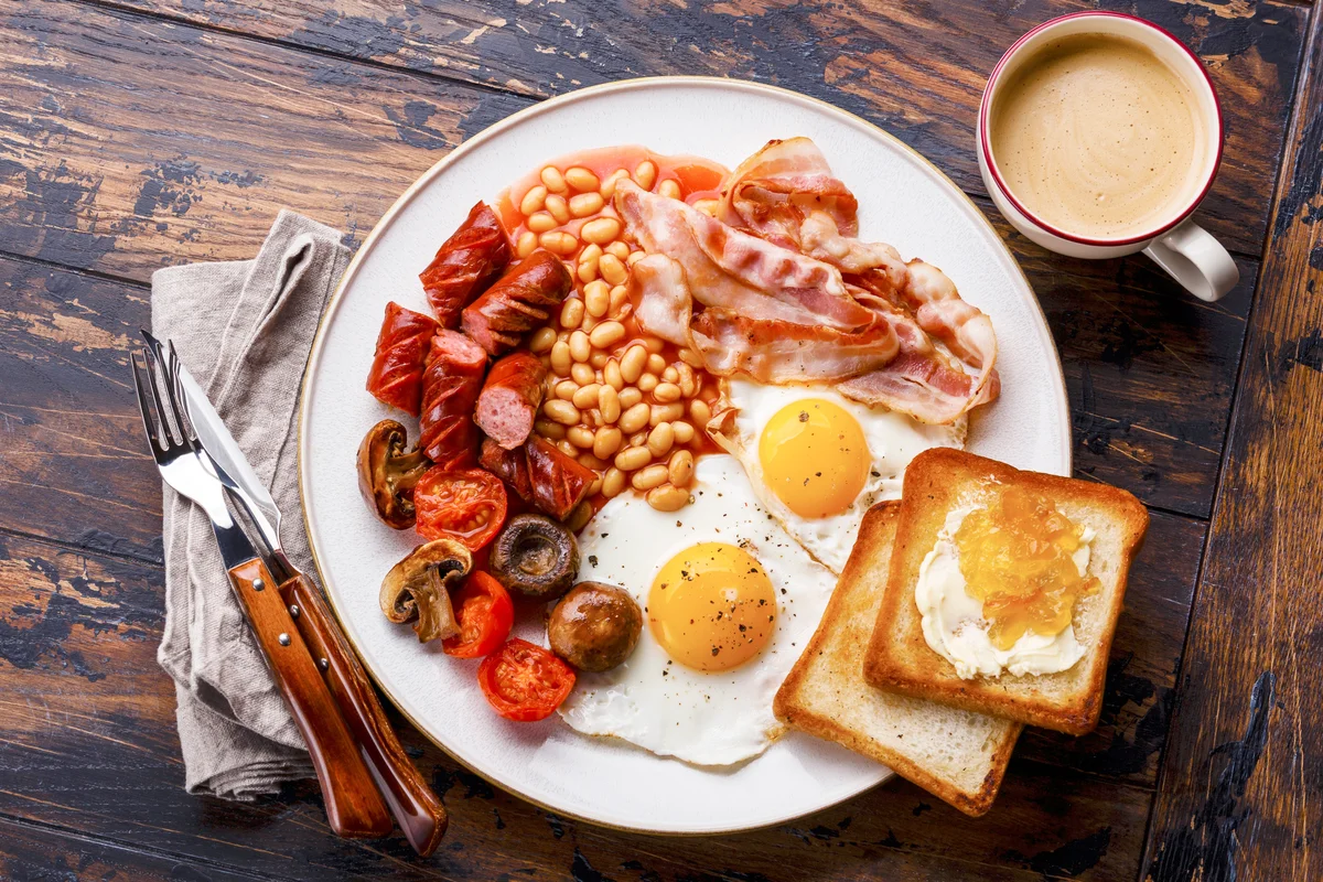 English breakfast with fried eggs, sausages, bacon, beans, toasts and coffee