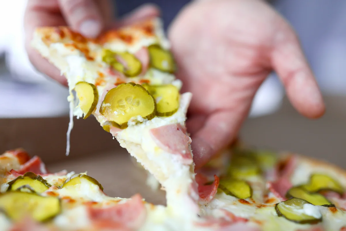 Man holding a slice of pizza with pickles