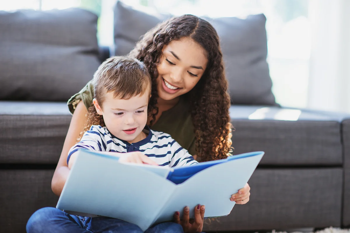 Babysitter and kid spending time reading a book together in the living room