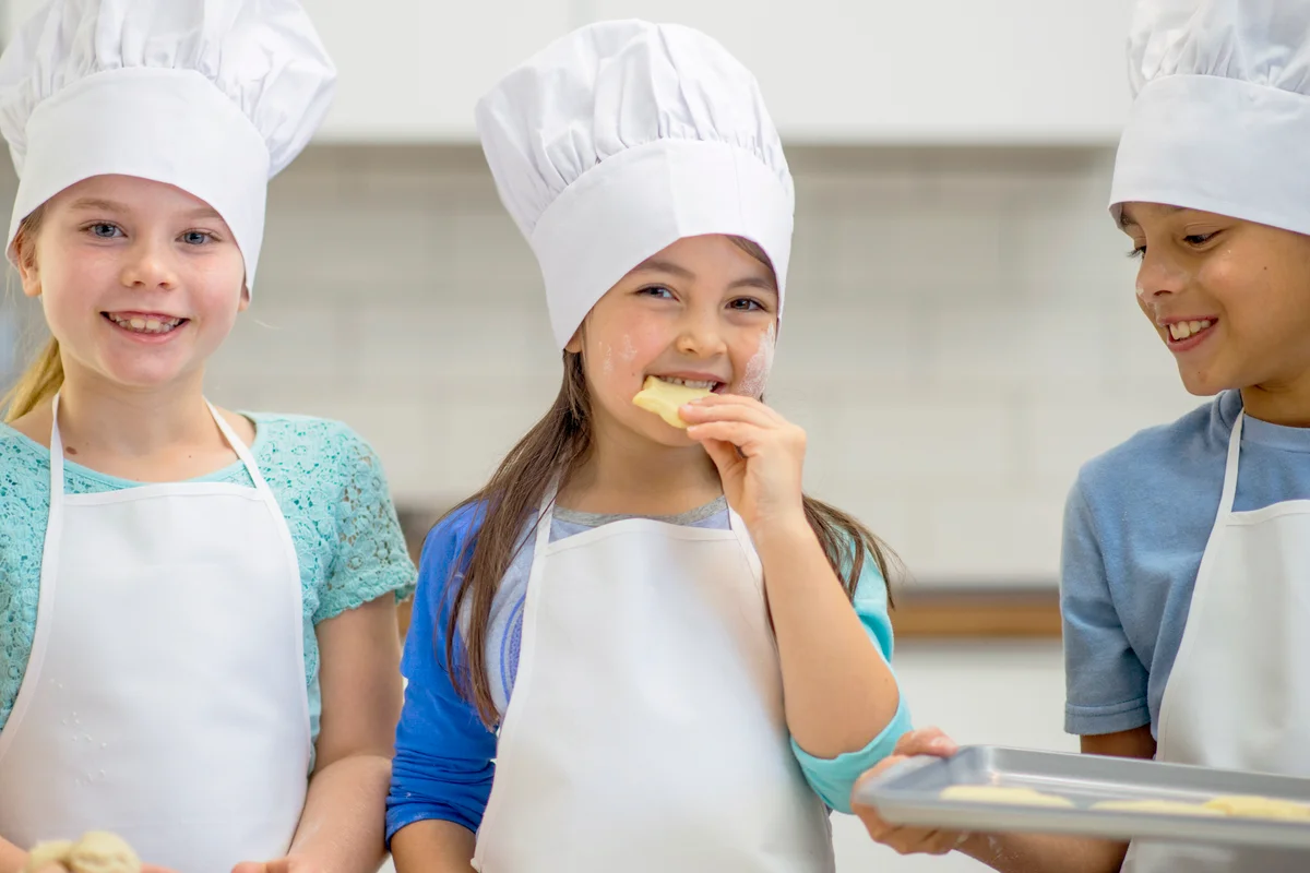 Kids wearing aprons and chefs hats while making cookies