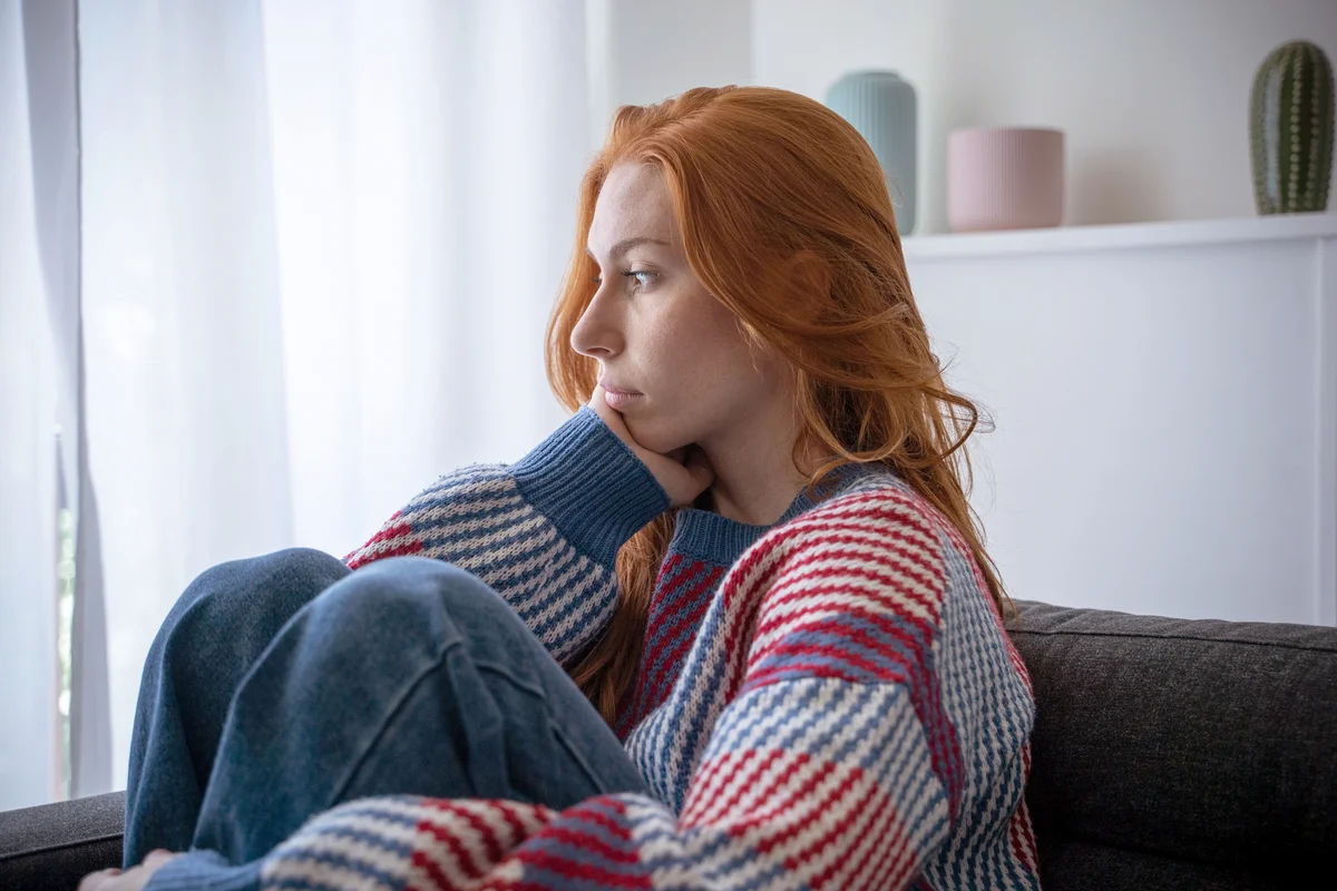 Pensive woman sitting on sofa feeling blue