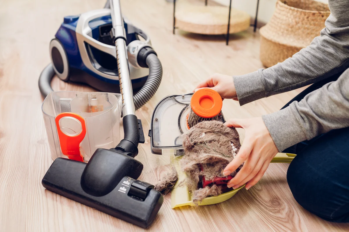 Woman removes garbage from dust filter of vacuum cleaner at home