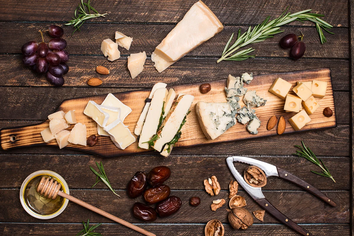 Cheese platter with different cheeses, grapes, nuts, honey, bread and dates on rustic wooden background