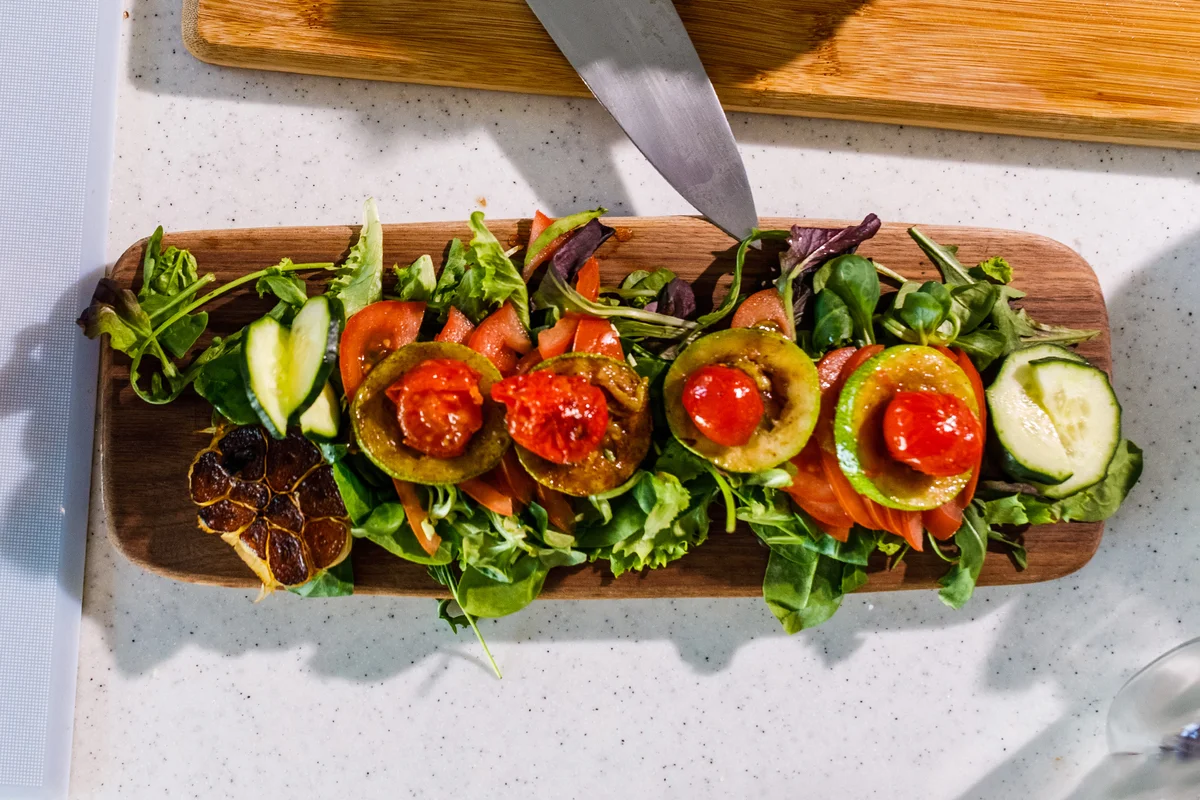 bed of mixed greens, tomatoes, cucumbers, roasted garlic, grilled zucchinis and roasted cherry tomatoes on a board