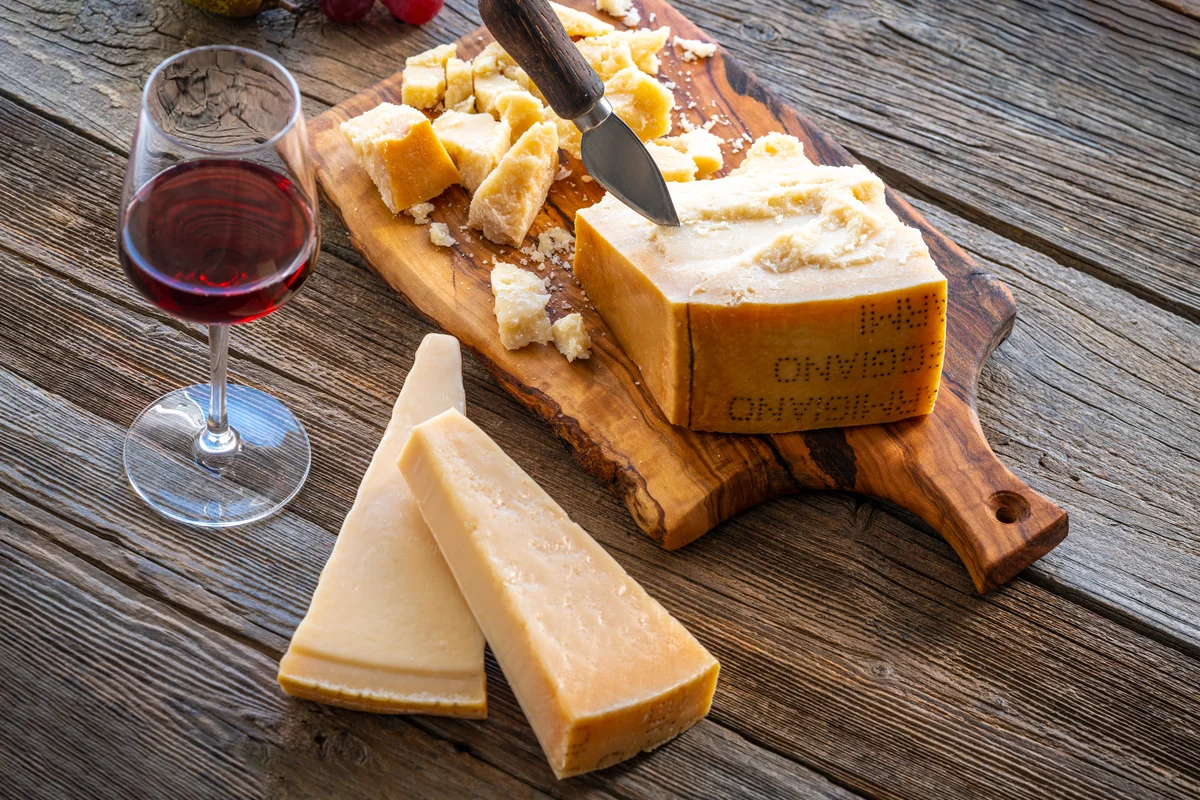 Parmesan Reggiano cheese on cutting board knife with wine and fruits on table