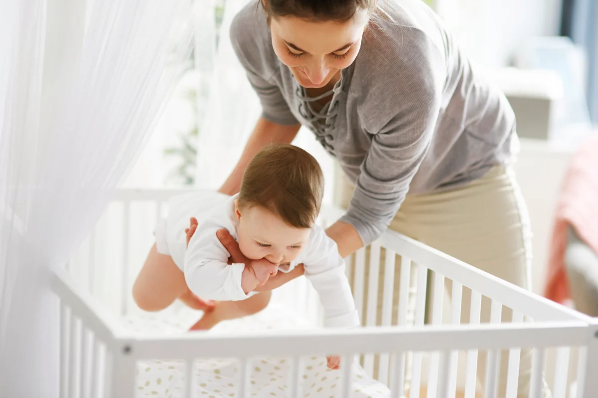 Mother laying her baby into crib