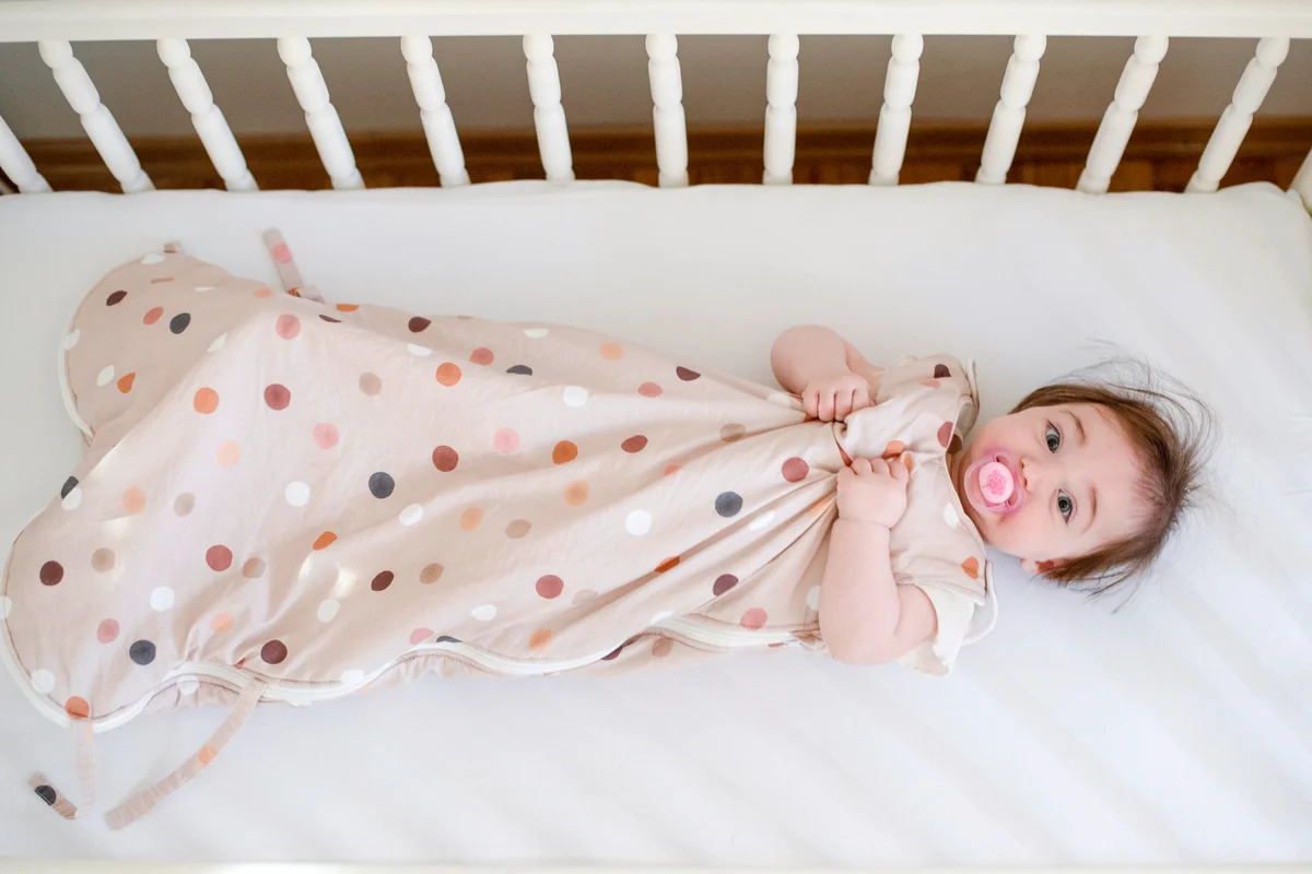 Baby in sleeping bag laying down in a crib