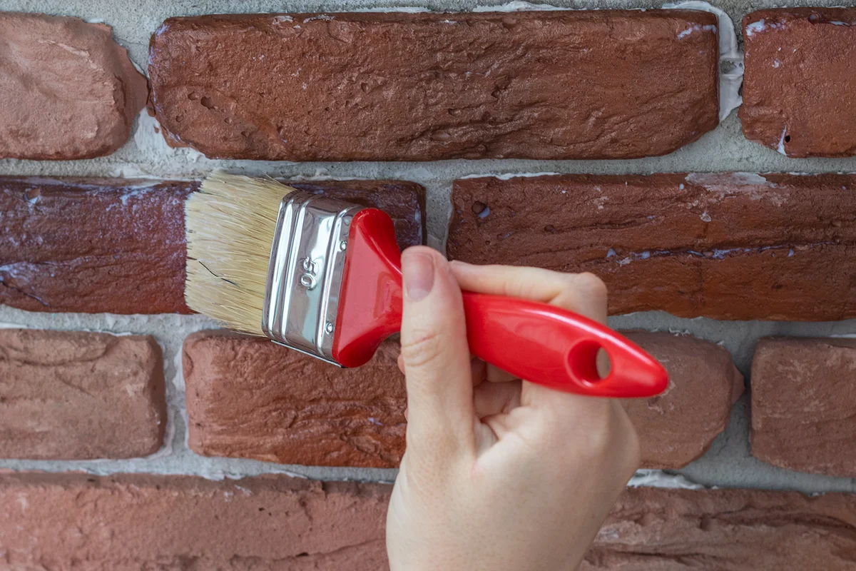 Female hand applies varnish to decorative facing brick