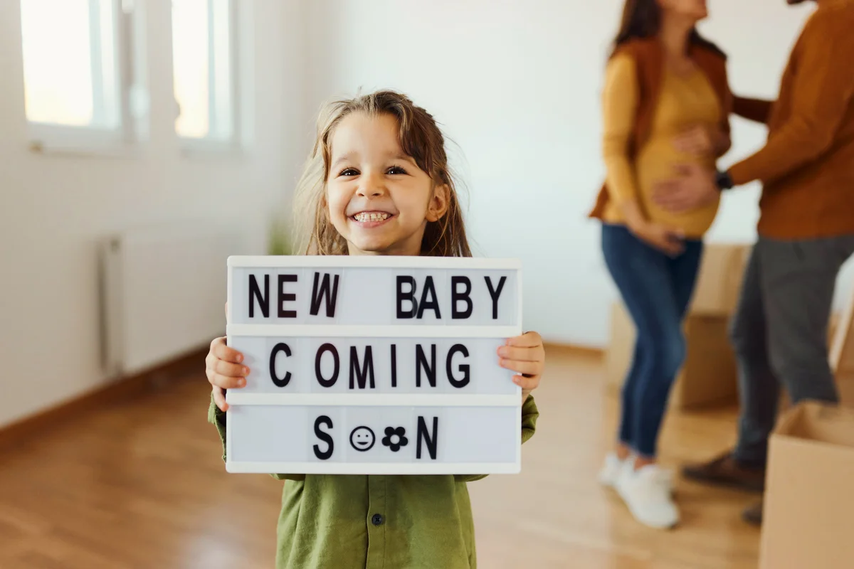 Happy little girl holding announcement message with a text that new baby is coming soon