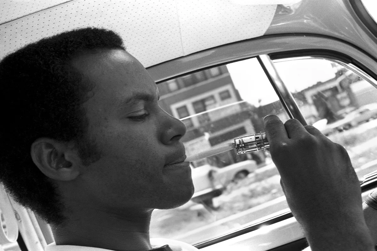 Robert Abbott Sengstacke, using a car lighter to light a cigarette while driving, Chicago, Illinois, mid to late 1960s