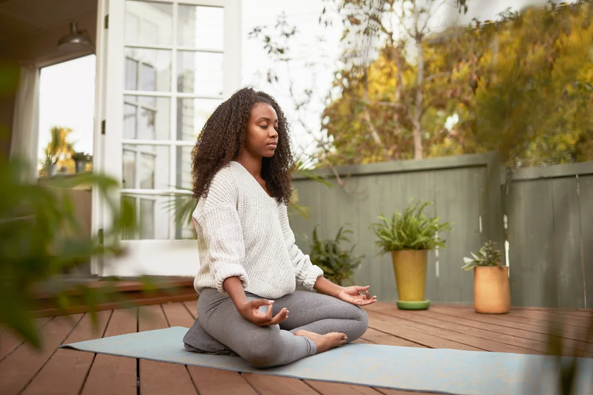 Young woman sitting in the lotus pose outside on her patio